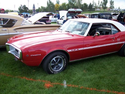 1972 Ford Ranchero - A red 1969 Pontiac Firebird convertible with a white top is parked on the grass at an outdoor car show.