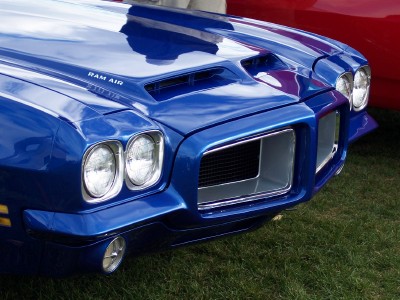 1972 Ford Ranchero - The front grille and dual headlights of a bright blue muscle car are visible, with a red vehicle in the background.