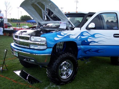 1972 Ford Ranchero - A modified pickup truck with custom flame paint and an open hood is displayed at an outdoor event.