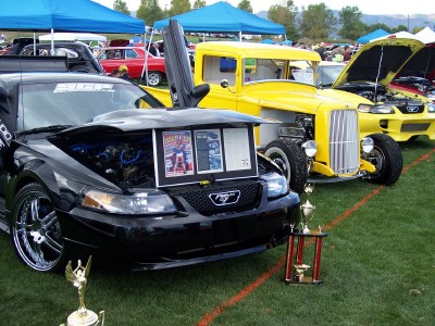 1972 Ford Ranchero - Multiple vehicles on display at an outdoor car show, including a black Mustang and a yellow hot rod truck.