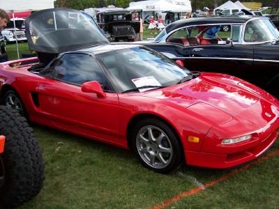 1972 Ford Ranchero - A red sports car is parked on grass at an outdoor car show, with a black classic car behind it.
