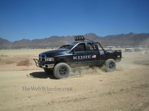 1990 Ford Bronco - black Dodge Ram off-road race truck marked KORE and numbered 861 races across a dusty desert course.
