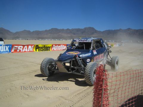 1990 Ford Bronco - blue tube-frame off-road race buggy sits on the desert beside FRAM and Autolite sponsor banners.
