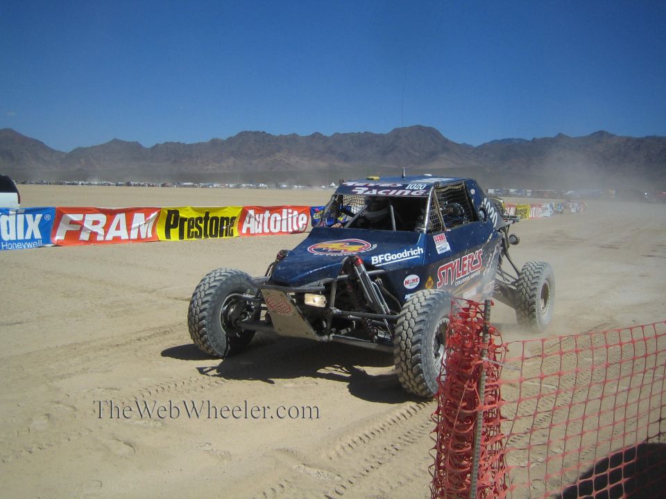 Blue off-road race buggy parked in desert near sponsor banners