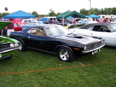 1972 Ford Ranchero - A black Plymouth Barracuda is displayed at an outdoor car show with other vehicles and tents in the background.