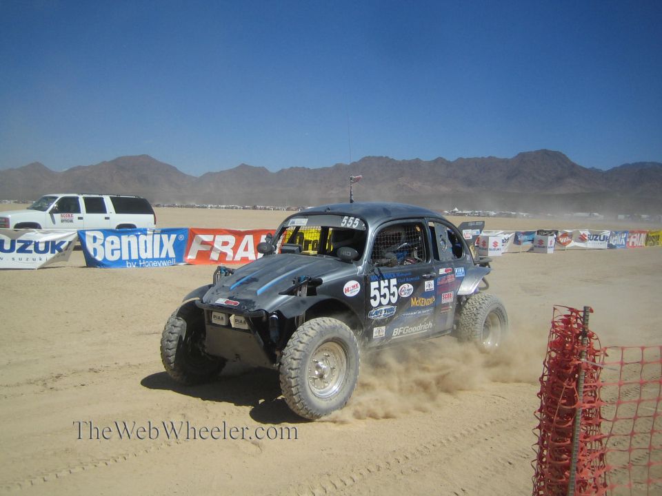 Black Baja Bug #555 on a desert course near sponsor banners