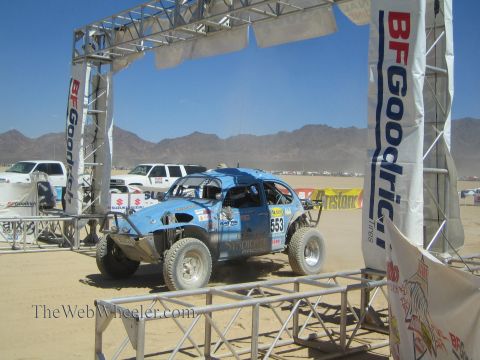 1990 Ford Bronco - blue VW Beetle-based Baja Bug numbered 553 sits beneath a BFGoodrich start arch on a desert course.