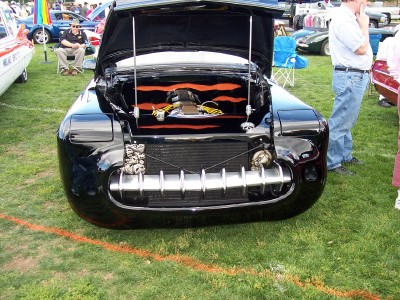1972 Ford Ranchero - A custom black car with its hood open displays a unique chrome grille and engine bay decoration at an outdoor car show.
