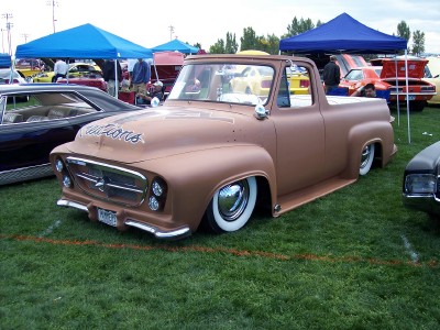 1972 Ford Ranchero - Customized pickup truck with a matte brown finish and chrome accents sits low on the grass at an outdoor car show.