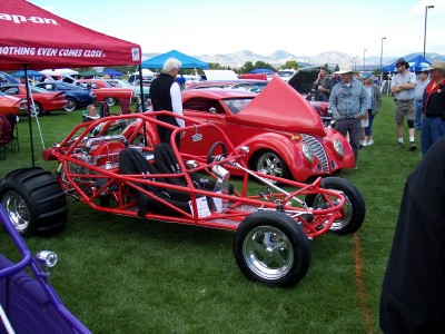 1972 Ford Ranchero - A red dune buggy and a red hot rod are displayed at an outdoor car show with spectators.