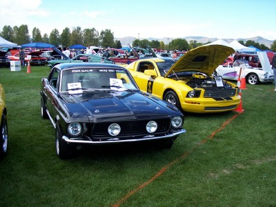 1972 Ford Ranchero - Two cars, a black classic and a yellow modern one, are displayed on a grassy field at an event.