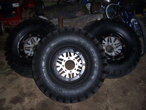 1983 Ford Bronco - Several large off-road tires with custom rims are displayed in a garage setting, with other items in the background.