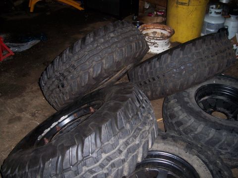1983 Ford Bronco - Several large off-road tires and rims are piled up in a garage setting.