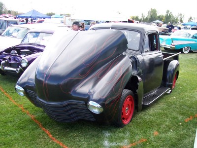 1972 Ford Ranchero - A custom black pickup truck with flame decals and red wheels is displayed at an outdoor car show.