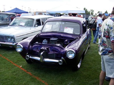 1972 Ford Ranchero - A custom purple sedan is displayed with its hood open at an outdoor car show, revealing the engine compartment.