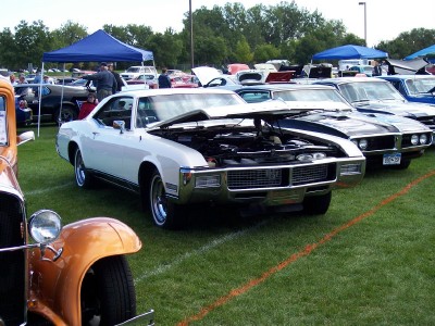 1972 Ford Ranchero - Several cars are displayed on a grassy field, with one white car prominently showing its open engine compartment.