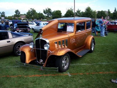 1972 Ford Ranchero - A custom hot rod sedan with an open hood is displayed at an outdoor car show with other vehicles and attendees.