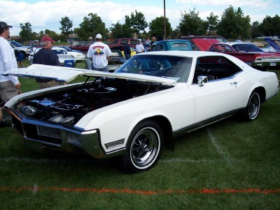1972 Ford Ranchero - A white 1971 Buick Riviera is displayed with its hood open at an outdoor car show, surrounded by other vehicles.