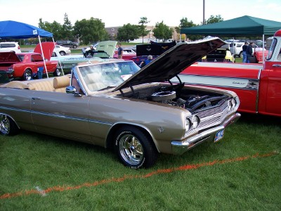 1972 Ford Ranchero - A tan convertible with its hood open sits on display at an outdoor car show, parked next to a red truck.