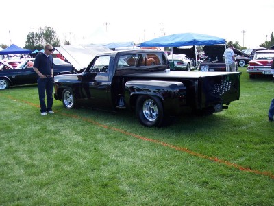 1972 Ford Ranchero - A black pickup truck is displayed on a grassy field at an outdoor event with other vehicles present.