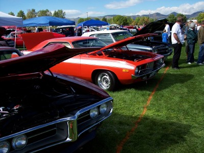 1972 Ford Ranchero - A red muscle car with a white stripe is displayed at an outdoor car show, with other vehicles and spectators in the background.