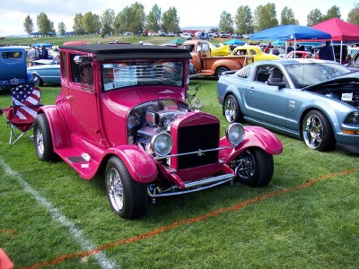 1972 Ford Ranchero - A pink hot rod coupe is parked on grass next to a modern blue car at an outdoor car show.