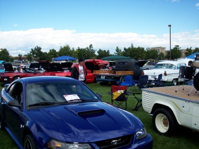 1972 Ford Ranchero - A blue Ford Mustang is prominently displayed at a car show, with other vehicles and tents in the background under a partly cloudy sky.
