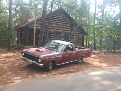 1966 Ford Ranchero - A 1966 Ford Ranchero sits in front of a rustic log cabin in a wooded area.