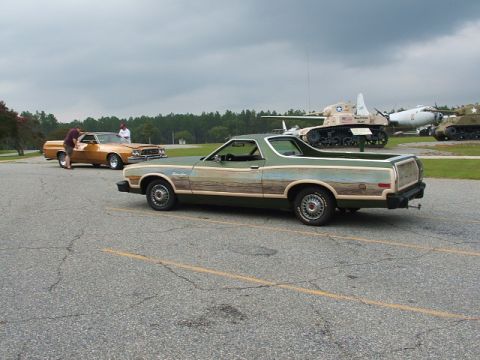 1966 Ford Ranchero - A green Ford Ranchero with wood paneling is parked next to another car, with military vehicles in the background.