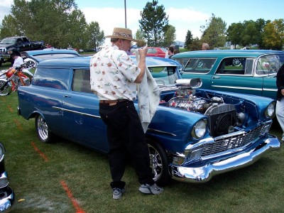 1972 Ford Ranchero - A man cleans the engine bay of a blue panel van at an outdoor car show.