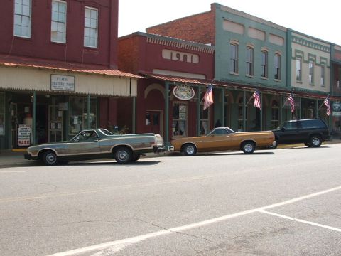 1966 Ford Ranchero - Two Ford Rancheros and a black SUV are parked along a street in front of vintage buildings. The green Ranchero is likely a 1977 model.
