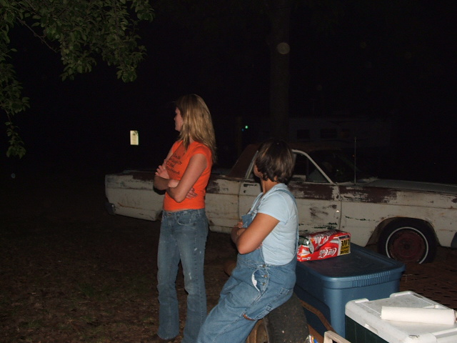 1966 Ford Ranchero parked outside at night, showing its side profile. Two people stand nearby