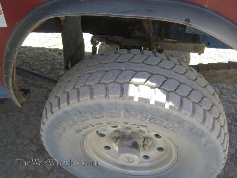1990 Ford Bronco - dusty BFGoodrich tire on a steel wheel sits under the red fender of an off-road truck parked on dry cracked earth.