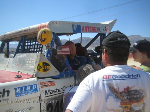 1990 Ford Bronco - Spectators crowd around a blue desert off-road race truck marked Antenex and FNJeep, one wearing a BFGoodrich Winner shirt.
