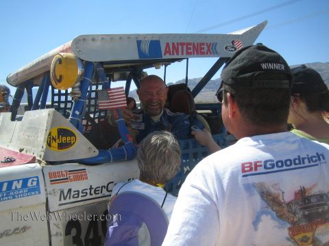 1990 Ford Bronco - grinning driver in a blue race suit reaches out from a blue Antenex off-road truck as fans in BFGoodrich shirts gather around.