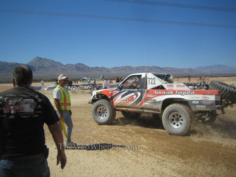 1990 Ford Bronco - red and white Norwalk Toyota number 722 off-road race truck kicks up dust on a desert course as spectators and a marshal watch.