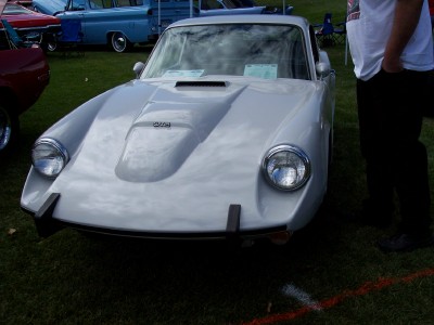 1972 Ford Ranchero - A light-colored sports car is parked on grass at an outdoor event with other vehicles in the background.