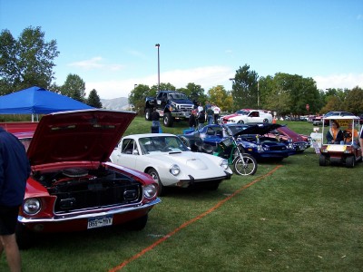 1972 Ford Ranchero - Outdoor car show features a variety of vehicles including a 1972 Ford Mustang and a white sports car.