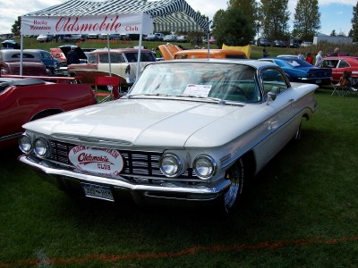 1972 Ford Ranchero - A white 1959 Oldsmobile is displayed at a car show under a tent with other vehicles in the background.
