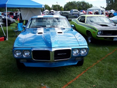 1972 Ford Ranchero - A blue 1970 Pontiac Firebird is displayed at an outdoor car show next to a green muscle car.