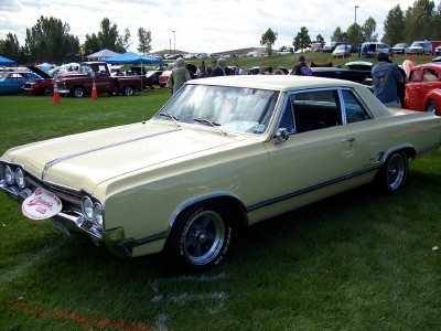 1972 Ford Ranchero - A pale yellow 1965 Oldsmobile 442 coupe is displayed on a grassy field at an outdoor car show.