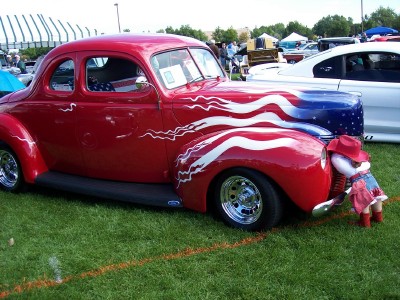 1972 Ford Ranchero - A classic red coupe with patriotic paint is displayed on a grassy field next to a white car.