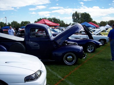 1972 Ford Ranchero - A dark blue pickup truck is displayed with its hood open at an outdoor car show, alongside other vehicles.