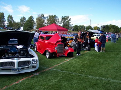 1972 Ford Ranchero - A white car with its hood open is displayed at an outdoor car show, with other vehicles and people in the background.