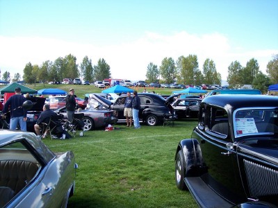 1972 Ford Ranchero - A classic black car with a sign on its windshield is displayed at an outdoor car show with other vehicles and tents in the background.