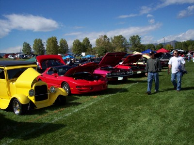 1972 Ford Ranchero - Several cars are parked on a grassy field under a blue sky with scattered clouds.