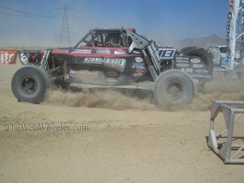 1990 Ford Bronco - black single-seat off-road race buggy with Castro and Toyota livery kicks up dust racing across a desert course.