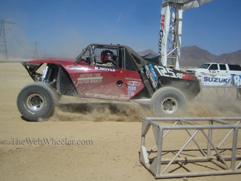 1990 Ford Bronco - maroon off-road race buggy numbered 125 with Motion Tire Motor Sports livery races over a dusty desert track.