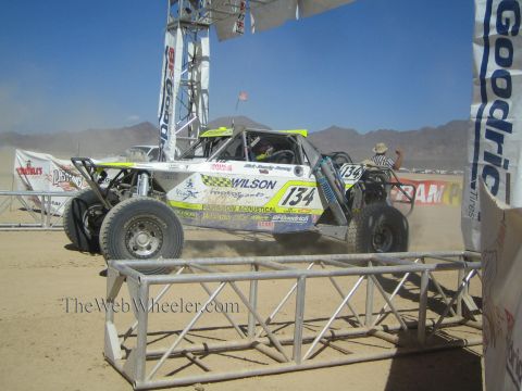 1990 Ford Bronco - white and green off-road race buggy numbered 134 with Wilson livery sits at a desert start line under a BFGoodrich arch.