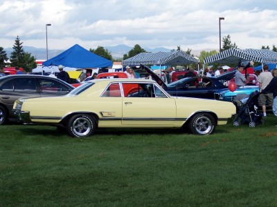 1972 Ford Ranchero - A pale yellow coupe with a distinctive body style is displayed at an outdoor event with other vehicles and tents.